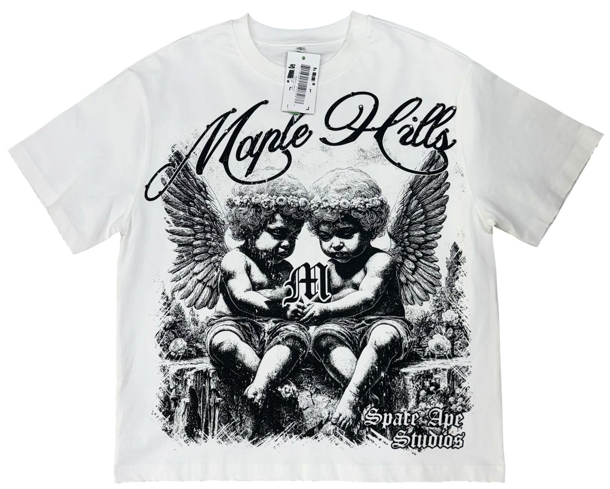 A white short-sleeve graphic t-shirt featuring a black and white illustration of two cherubs with wings, the text 'Maple Hills' in cursive, and 'Spade Eye Studios' at the bottom. A hangtag is visible at the collar.